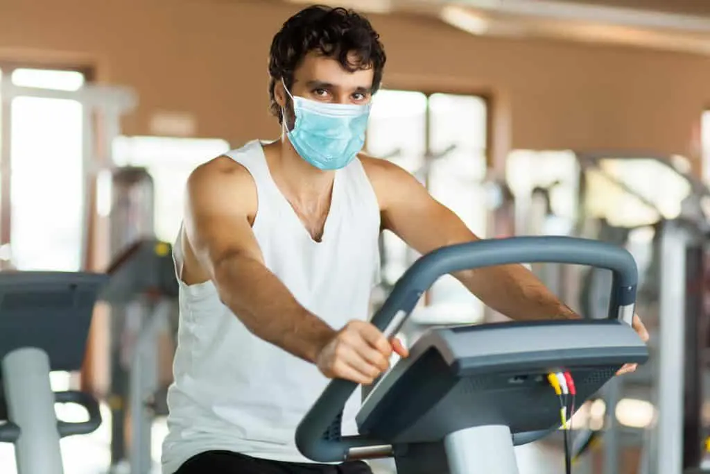 Man in the gym, exercising his legs doing cardio training on bicycle wearing a mask - coronavirus concept